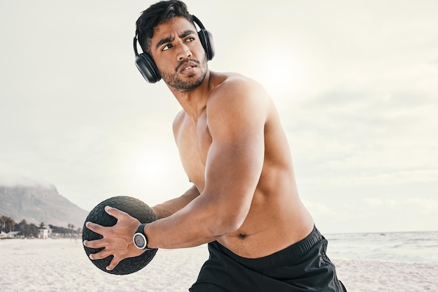 Foto música y ejercicio, ahora que es una buena combinación. una foto de un joven deportivo que usa audífonos mientras hace ejercicio al aire libre con un balón medicinal.