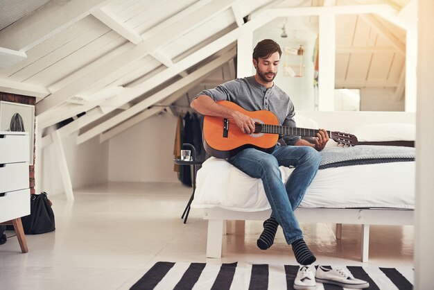 La música es su pasión Foto de un apuesto joven practicando guitarra en casa