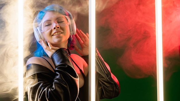 Música escalofrío Lista de reproducción alegría Gadget futurista Mujer alegre satisfecha en auriculares escuchando la canción en luz de neón roja LED sobre fondo de espacio de copia de humo oscuro