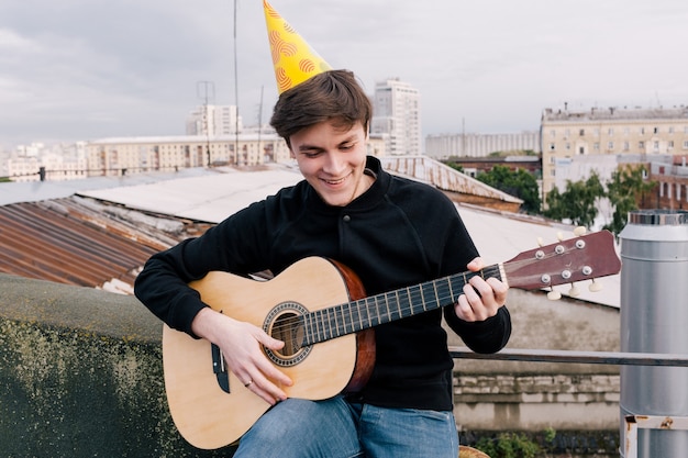 Música en la fiesta de cumpleaños. Celebración en la azotea. Joven guitarrista festivo al aire libre