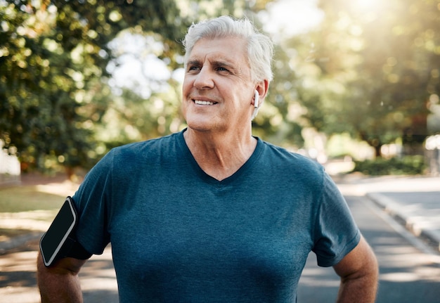 Música de fitness y correr con un anciano en el parque con auriculares para hacer ejercicio por la mañana y deportes Tecnología Freedom y bienestar con un corredor en el vecindario con una aplicación de podcast y teléfono