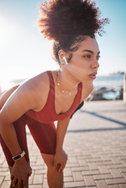 Música fitness e cansada com uma corredora negra no calçadão para treinamento aeróbico ou de resistência Exercícios de corrida e fones de ouvido com uma esportista se sentindo exausta durante o treino