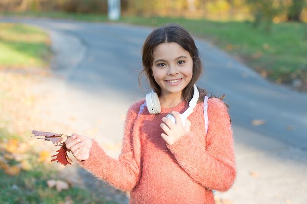 Música de hojas de otoño Niña feliz usa auriculares en el paisaje otoñal Sonrisa de niño lindo con auriculares estéreo de oído Niño pequeño con auriculares modernos Tecnología de auriculares