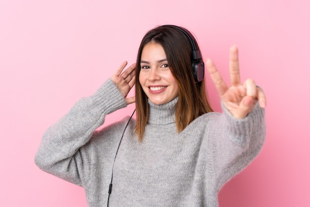 Música jovem com fones de ouvido sobre parede rosa isolada