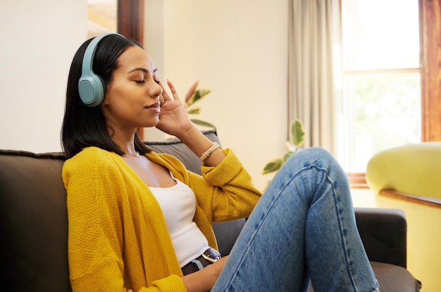 Música de mujer y relajación con auriculares en el sofá de la sala de estar disfrutando de una relajación tranquila en casa Mujer joven relajándose en un sofá escuchando una pista de audio relajante en la casa para aliviar el estrés