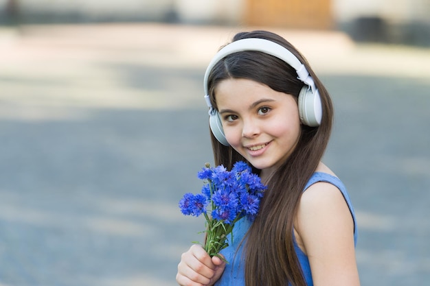 Música para seus ouvidos bebê feliz com flores ouvir música menina usa fones de ouvido tocando música férias de verão nova tecnologia vida moderna diversão e entretenimento deixe a música te levar