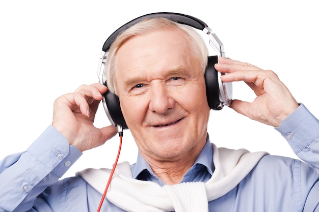 Música para todas as idades. Retrato de homem sênior em fones de ouvido, ouvindo música e sorrindo em pé contra um fundo branco