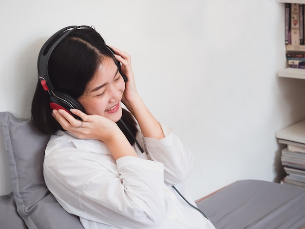 Música que escucha de la muchacha asiática en auriculares en cama