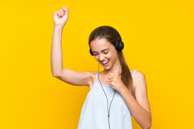 Música que escucha de la mujer joven aislada en la pared amarilla que celebra una victoria