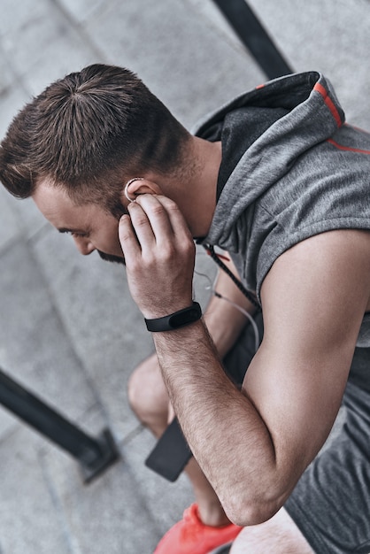 la música siempre lo motiva. Apuesto joven en ropa deportiva ajustando sus auriculares