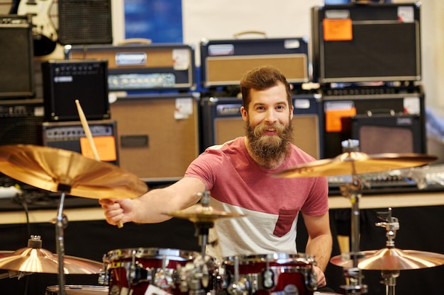 Foto música, venda, pessoas, instrumentos musicais e conceito de entretenimento - músico masculino tocando pratos no kit de bateria na loja de música