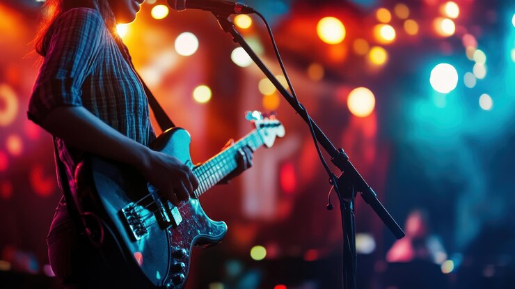 Un músico actúa en el escenario Una persona toca una guitarra eléctrica y canta en un micrófono en una sala de conciertos brillantemente iluminada Las figuras borrosas de una audiencia llenan el fondo