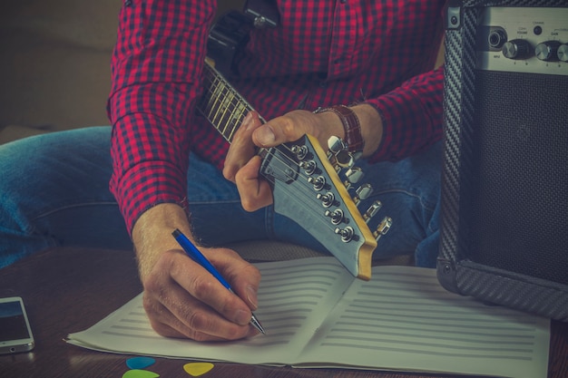 Músico de hipster senta-se no sofá com uma guitarra e grava as notas de sua melodia