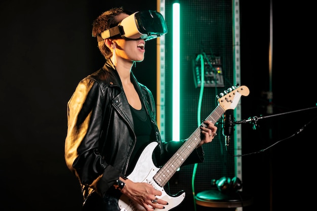 Músico de mulher tocando guitarra elétrica no estúdio de som enquanto usava fone de ouvido de realidade virtual para simulação de concerto, curtindo a performance musical. Artista rebelde trabalhando em novo álbum de heavy metal