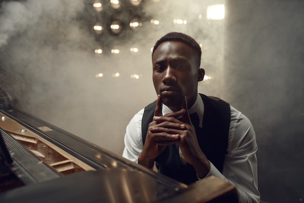 Músico de piano de cauda de ébano posa no palco com holofotes. pianista posa para um instrumento musical antes do concerto