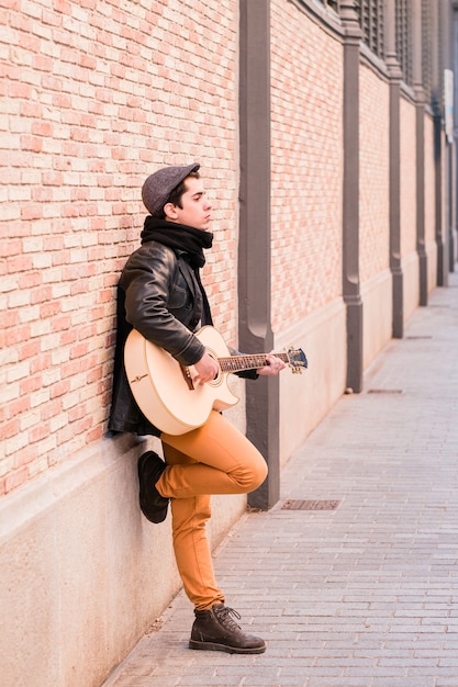 Músico de rua tocando violão. jovem bonito usando casaco e chapéu ao ar livre