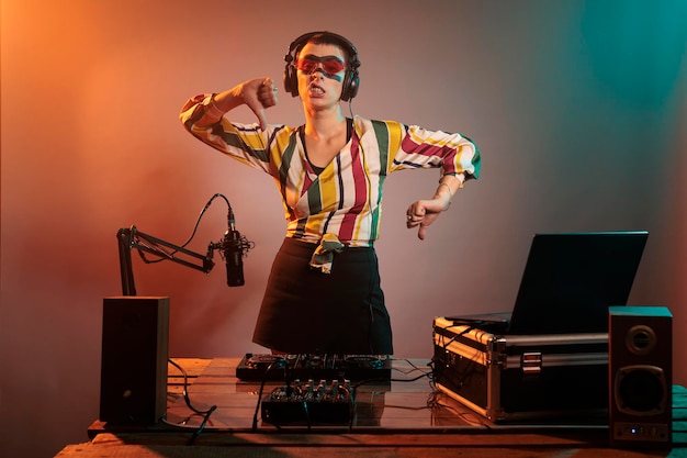 Músico feminino mostrando os polegares para baixo sinal em estúdio, fazendo gesto de desagrado e desaprovação depois de usar toca-discos e mixer para remixar música techno. Expressar rejeição e desacordo na festa.