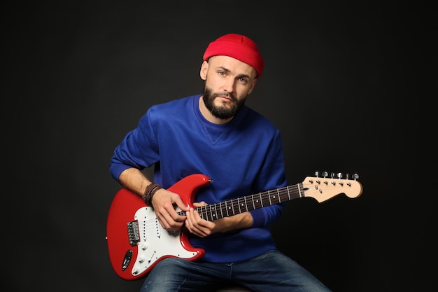 Músico hermoso joven que toca la guitarra en fondo negro