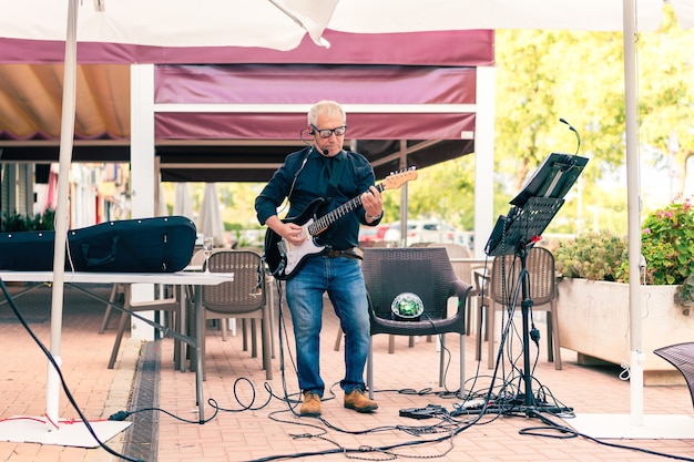 Músico idoso tocando guitarra elétrica em terraço com público