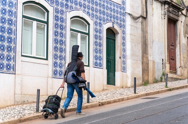 Foto músico itinerante com violão nas costas caminhando pelas ruas de lisboa portugal