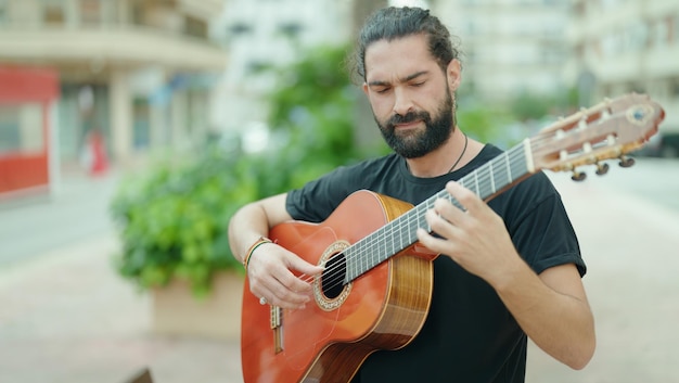 Músico jovem hispânico tocando violão clássico no parque