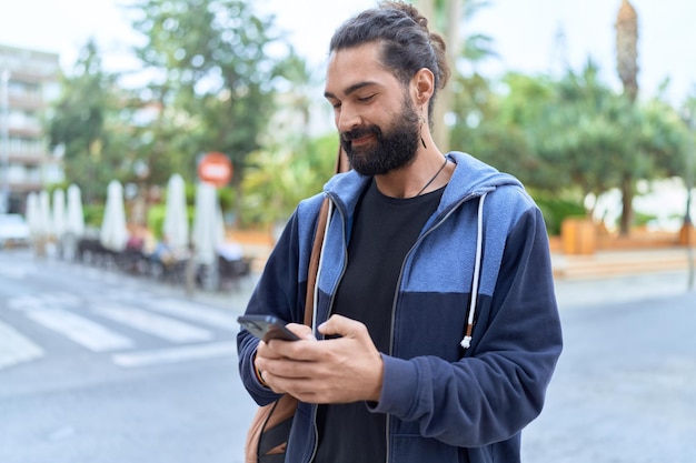 Músico jovem hispânico usando smartphone segurando caixa de guitarra na rua