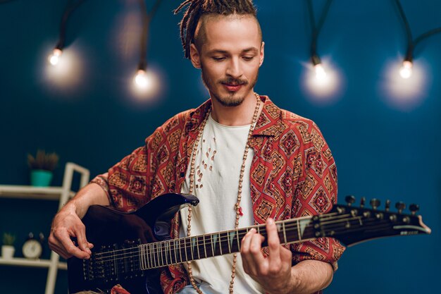 Músico joven chico elegante tocando la guitarra en su apartamento