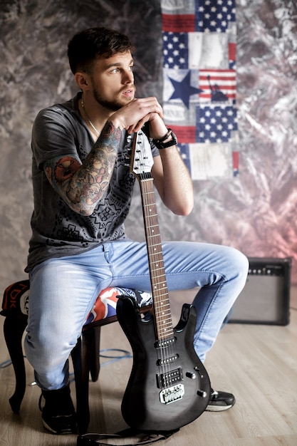 Foto músico joven guapo con guitarra eléctrica sobre un fondo oscuro