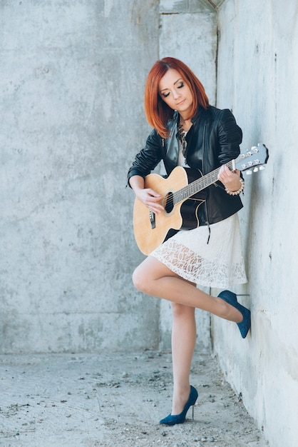 Músico joven con pelo rojo con una guitarra acústica