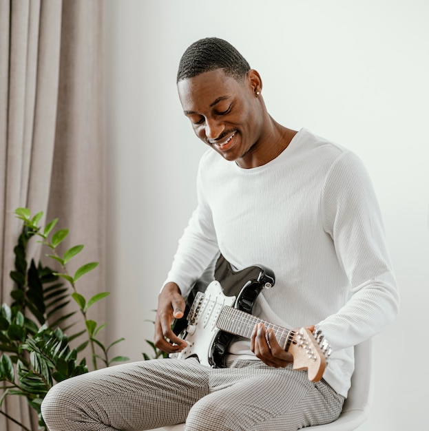 Músico masculino sonriente tocando la guitarra eléctrica en casa