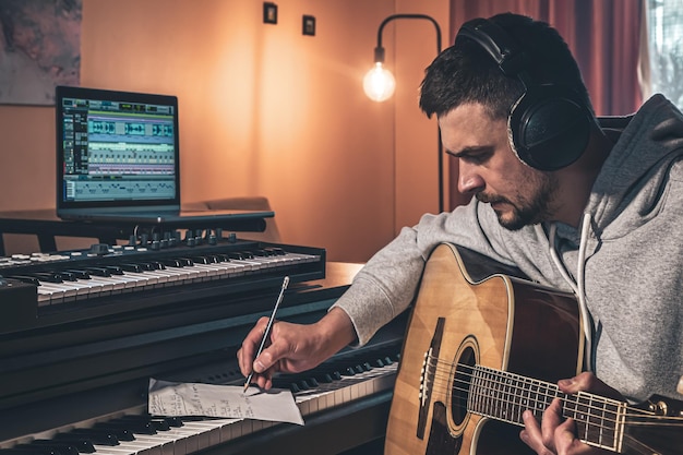 Músico masculino toca la guitarra en casa en el lugar de trabajo cerca de la computadora