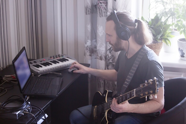 Músico tocando música e compondo uma música com guitarra elétrica, piano e laptop