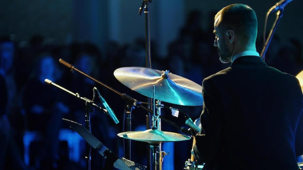 Un músico tranquilo disfrazado tocando la batería en el concierto de jazz Vista posterior