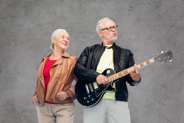 Musik, Alter und Menschen Konzept - glückliches Senior-Paar mit Elektro-Gitarre auf grauem Betongrund