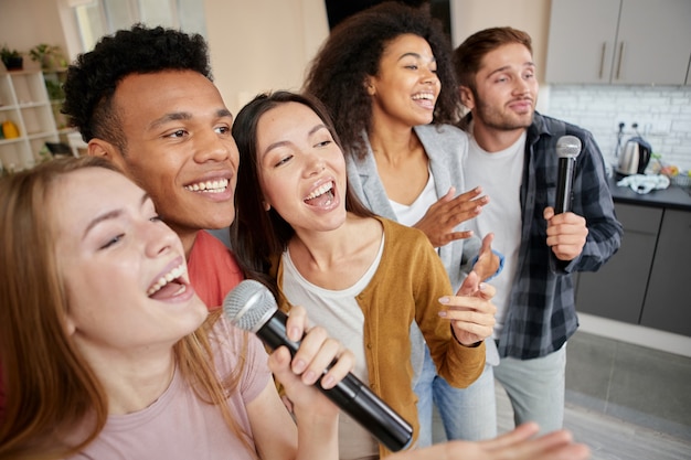 Musik für das Leben glückliche multikulturelle Freunde, die mit Mikrofon singen, während sie zu Hause Karaoke spielen
