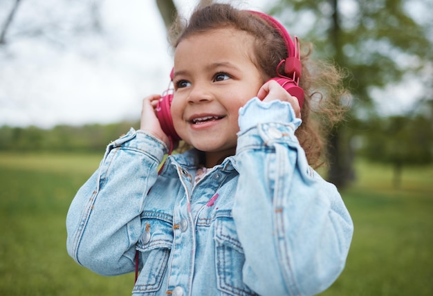 Musik, Lächeln und Baby in einem Park mit Kopfhörern, Radiofreiheit und Audio-Streaming in Portugal. Podcast glücklich und Gesicht eines jungen Kindes, das einem Lied für Glück, Freude und Fröhlichkeit in der Natur zuhört