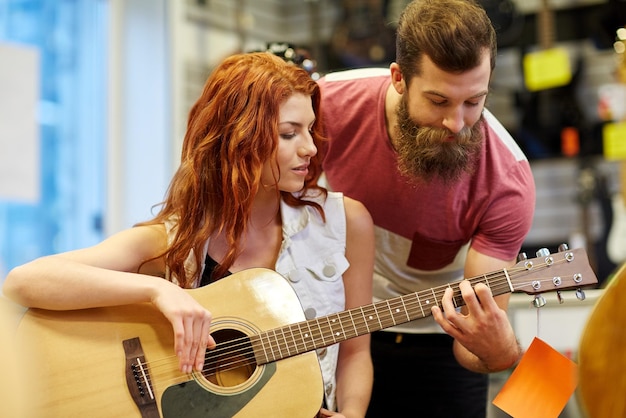 musik, verkauf, menschen, musikinstrumente und unterhaltungskonzept - glückliches musikerpaar mit gitarre im musikgeschäft