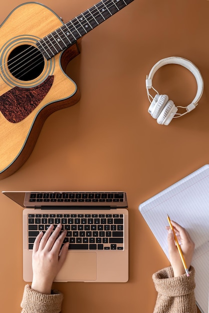 Musikalischer Hintergrund mit Akustikgitarre-Laptop und Draufsicht der weiblichen Hände