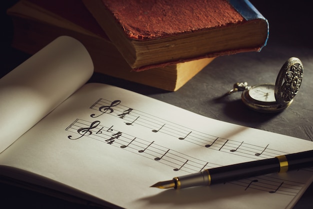 Musikanmerkungen und altes Buch mit Taschenuhr auf Holztisch.