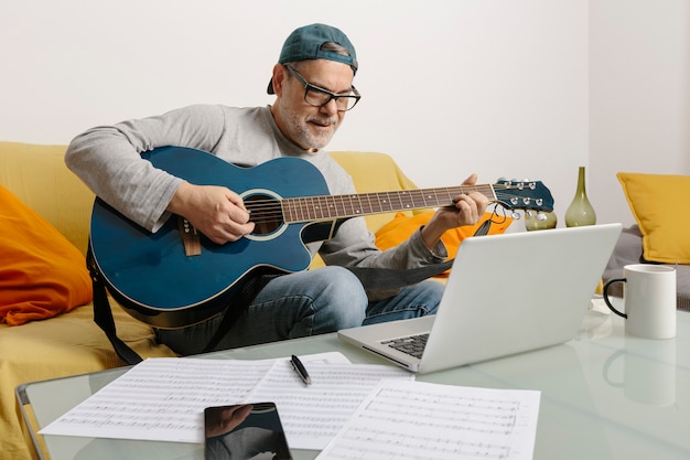 Musiker spielt Gitarre und komponiert mit seinen Kollegen per Videokonferenz über seinen Laptop