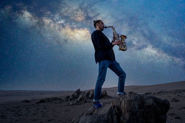 Musiker spielt Saxophon auf dem Gipfel des Berges mit Milky Way Hintergrund