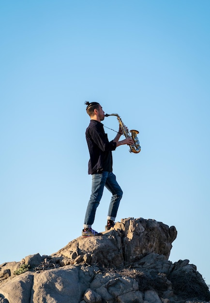 Musiker steht auf dem Felsen und spielt Saxophon bei Sonnenuntergang in der Wüste