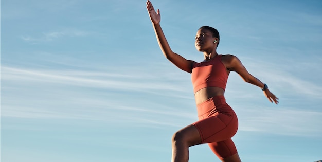 Musikkopfhörer für schwarze Frauen oder Laufen im Trainingstraining oder Übung für Marathon im Gesundheitswesen oder kardiovaskuläres Wohlbefinden Sport- oder Fitnessläufer mit niedrigem Winkel auf blauem Himmelshintergrund mit Radio