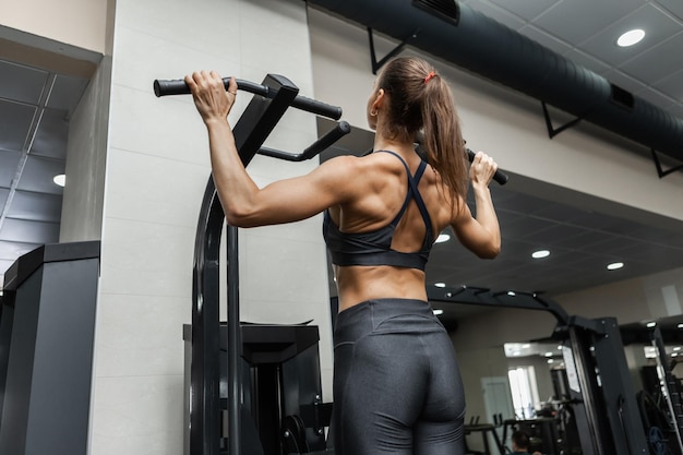 Muskulös fitte Frau zieht sich im Klimmzug-Trainingsgerät im Fitnessstudio hoch