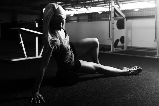 Muskulöse Frau dehnt sich mit Roller auf dem Boden in einem Fitnessstudio aus und lässt Muskeln spielen Muskulöser athletischer Bodybuilder Fitness-Modell