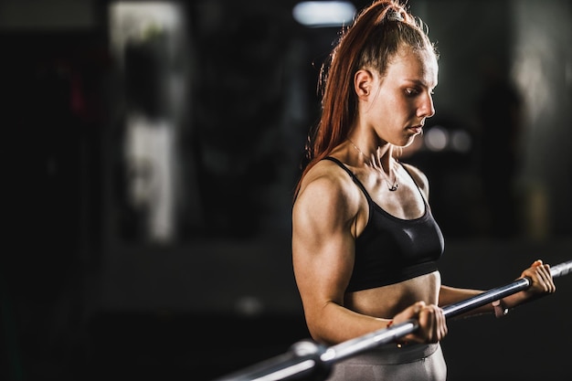 Muskulöse Frau, die beim harten Training im Fitnessstudio trainiert. Sie pumpt den Bizepsmuskel mit schwerem Gewicht auf.