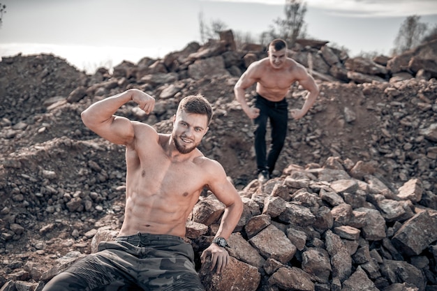 Muskulöse Jungs mit nacktem Oberkörper posieren mit angespannten Händen Outdoor-Foto Porträt eines gutaussehenden Mannes in dunklen Hosen