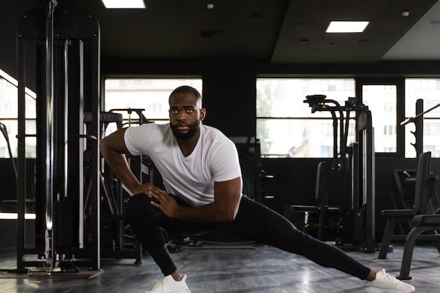 Muskulöser afrikanischer Mann im Fitnessstudio, der Dehnübungen auf dem Boden macht