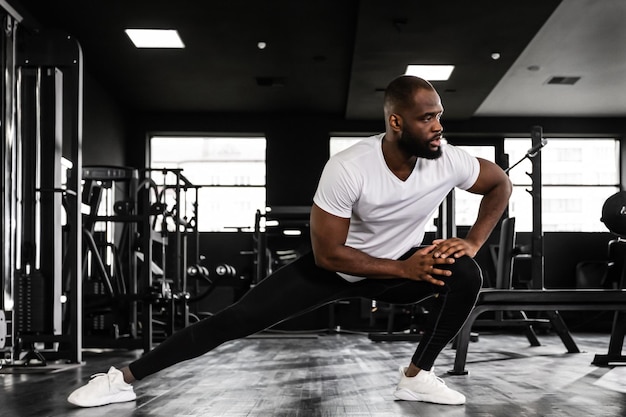 Muskulöser afrikanischer Mann im Fitnessstudio, der Dehnübungen auf dem Boden macht