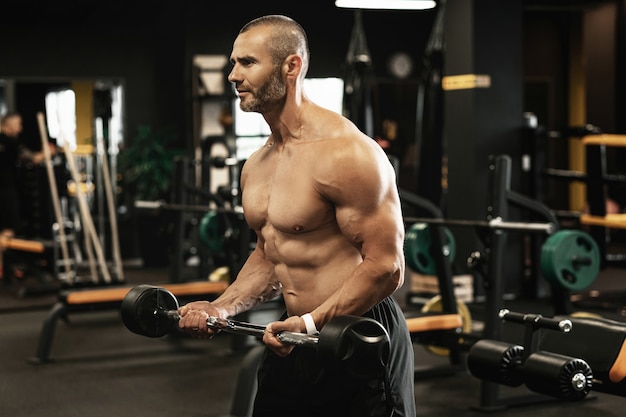 Muskulöser Bodybuilder, der während seines Trainings im Fitnessstudio Bizeps-Curls mit einer Langhantel macht